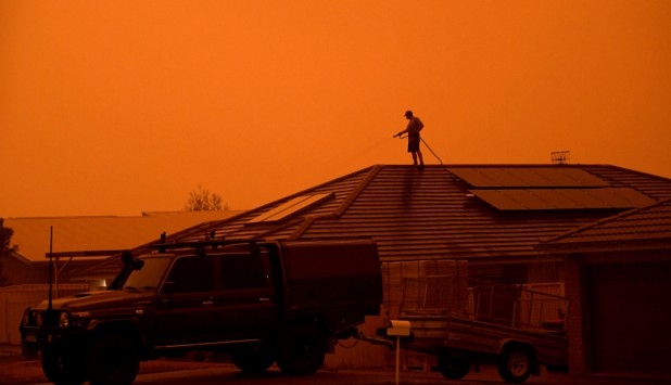 Un hombre usa una manguera para mojar su vivienda en un intento de evitar que sea afectada por los incendios. Foto: Reuters